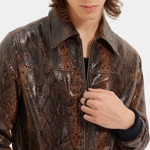 May include: A brown and black snakeskin patterned jacket with a pointed collar and a full-length front zipper. The jacket features long sleeves with dark ribbed cuffs and a textured finish that mimics the appearance of reptile scales throughout.