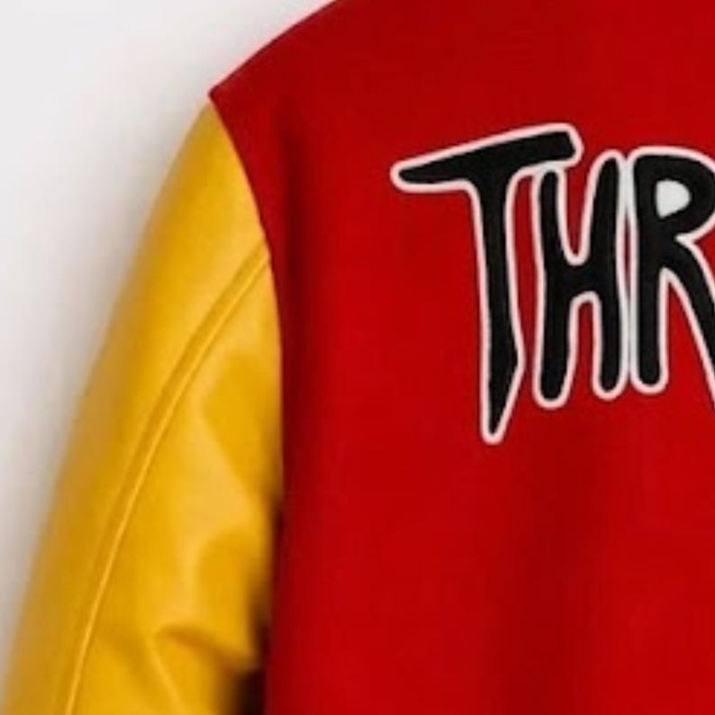 Puede incluir: Una chaqueta universitaria roja con mangas amarillas y el texto parcial THR bordado en negro con un contorno blanco sobre el cuerpo rojo. La chaqueta tiene una textura suave y un contraste claro entre la tela roja y las mangas amarillas.