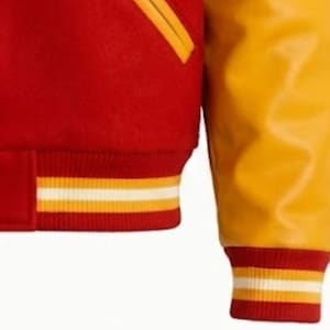 Puede incluir: Una chaqueta universitaria con cuerpo de mezcla de lana roja y mangas amarillas en contraste. La prenda incluye un dobladillo y pu&ntilde;os acanalados con rayas horizontales amarillas y blancas, junto con un bolsillo ribeteado en amarillo al frente.
