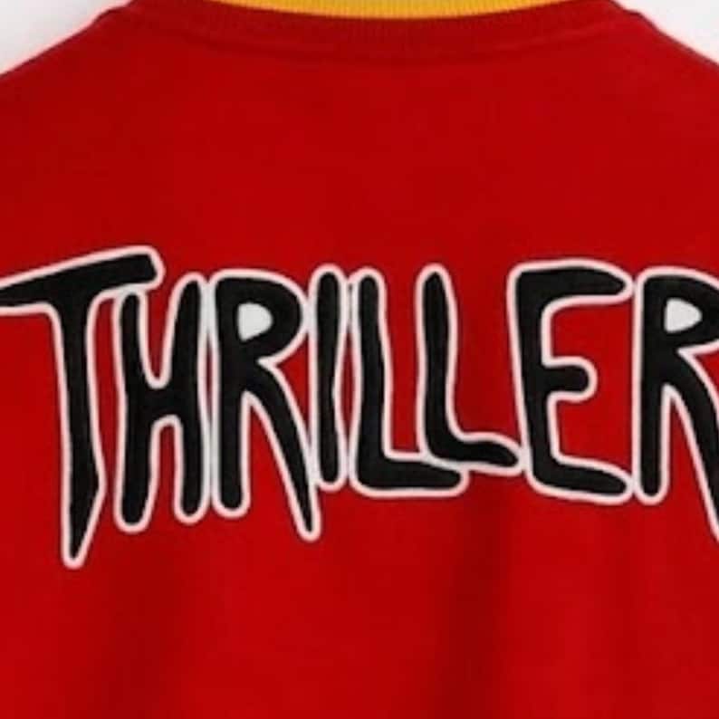 Puede incluir: Una sudadera de color rojo brillante con la palabra THRILLER bordada en letras negras gruesas con un borde blanco. La prenda tiene un cuello acanalado de color amarillo. El texto est&aacute; centrado y se extiende por la parte superior de la tela.