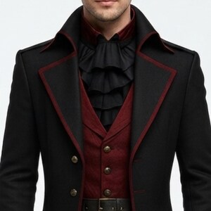 May include: A black coat with dark red piping along the lapels, worn over a dark red vest with metallic buttons. Underneath is a black shirt featuring a layered, ruffled jabot collar. The ensemble includes a black belt at the waistline.