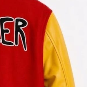 Puede incluir: Una chaqueta universitaria roja con mangas amarillas. El cuerpo rojo presenta una parte de letras negras con un contorno blanco. La chaqueta tiene una textura suave en el cuerpo y un acabado distintivo, ligeramente brillante en las mangas amarillas.