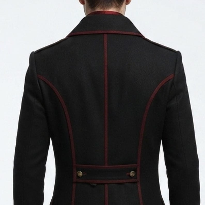 May include: A black jacket featuring dark red piping along the seams, a high collar, and a horizontal back tab detail with two metallic buttons. The garment is shown from the back, highlighting the structured paneling and the deep red trim.