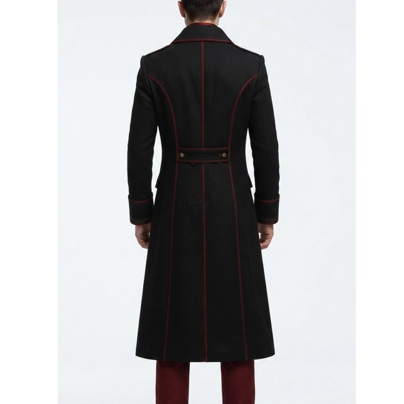 May include: A long black coat featuring structured seams highlighted by thin dark red piping. The coat includes a high collar, long sleeves with cuffs, and a horizontal back tab detail with two small metallic buttons at the waistline.