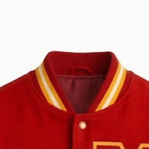 Puede incluir: Una chaqueta universitaria roja con cuello acanalado de rayas amarillas y blancas. La chaqueta est&aacute; confeccionada en un material similar al fieltro e incluye un cierre de bot&oacute;n a presi&oacute;n visible en la parte delantera, con forro interior rojo.