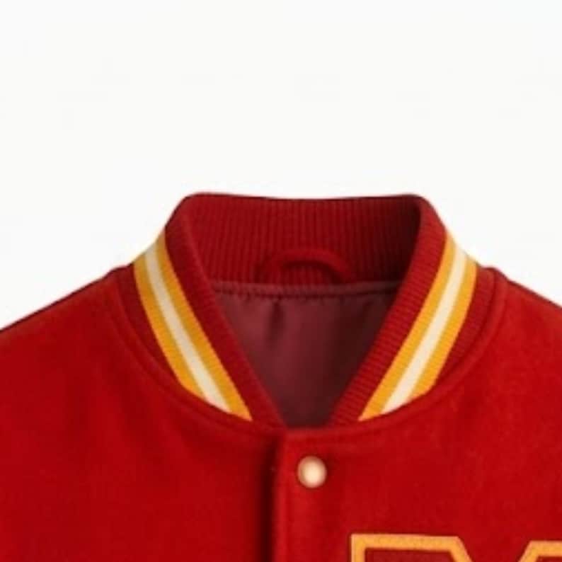 Puede incluir: Una chaqueta universitaria roja con cuello acanalado de rayas amarillas y blancas. La chaqueta est&aacute; confeccionada en un material similar al fieltro e incluye un cierre de bot&oacute;n a presi&oacute;n visible en la parte delantera, con forro interior rojo.