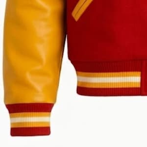 Puede incluir: Una chaqueta universitaria con cuerpo de mezcla de lana roja y mangas amarillas en contraste. La prenda incluye pu&ntilde;os y dobladillo acanalados, ambos detallados con rayas horizontales en blanco y amarillo. Se observa un borde de bolsillo amarillo.