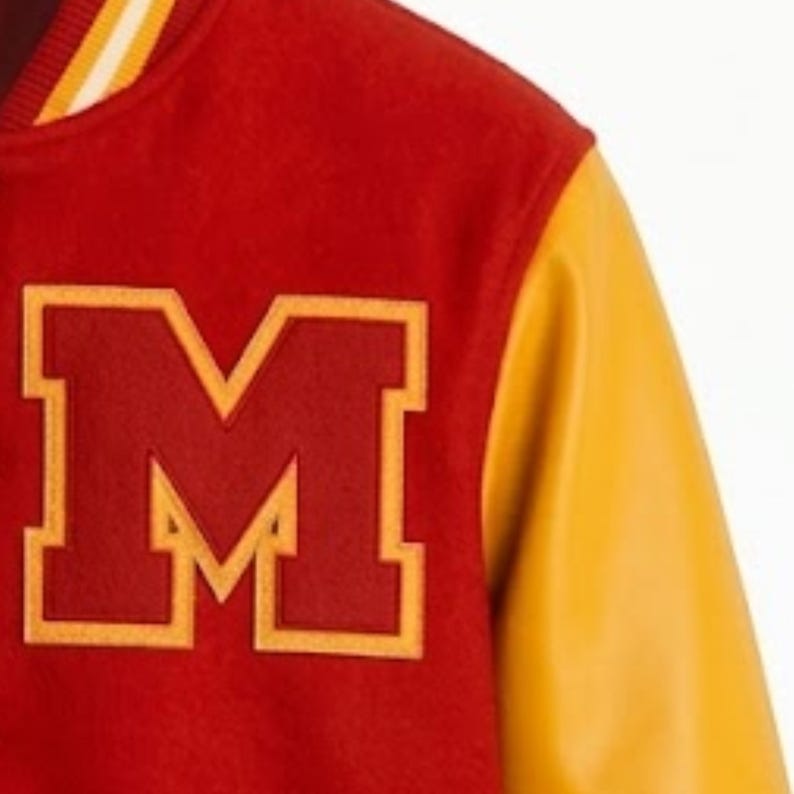 Puede incluir: Una chaqueta universitaria roja con una letra M grande de color rojo oscuro aplicada con un borde amarillo en el pecho. La chaqueta tiene mangas amarillas en contraste y un cuello acanalado con rayas amarillas y blancas, de dise&ntilde;o deportivo.