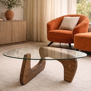 Puede incluir: Una mesa de centro con un tablero de cristal transparente de forma orgánica, sostenido por dos piezas de base de madera entrelazadas y teñidas de oscuro. La base está construida con madera maciza curvada con veta visible.