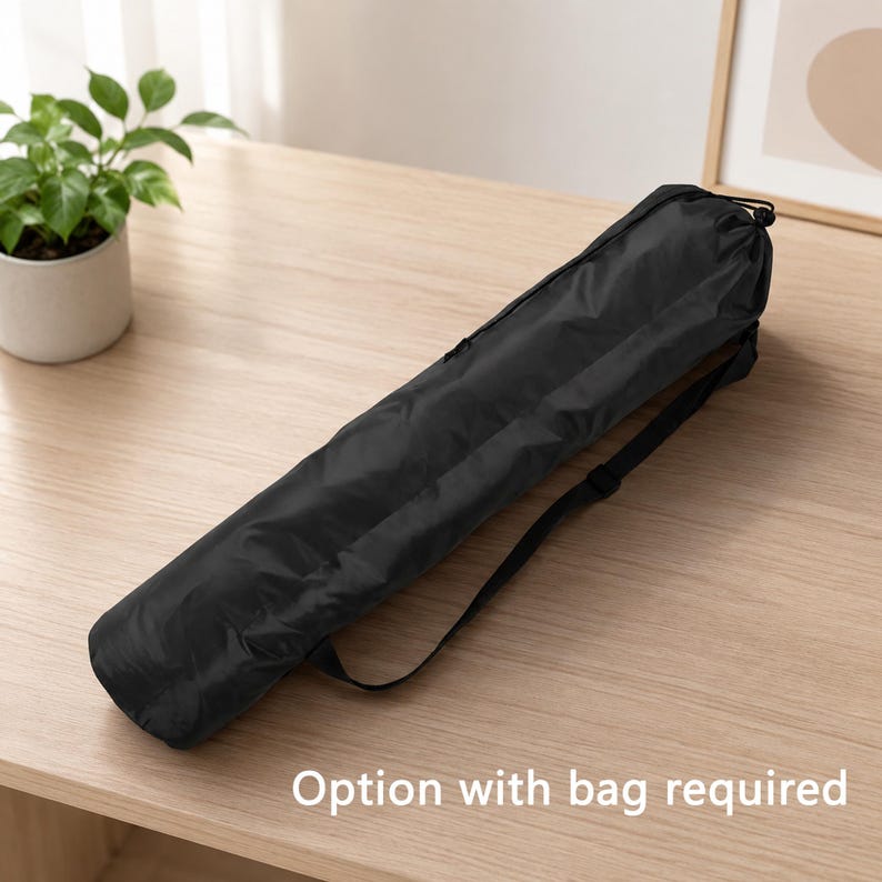 May include: A black, cylindrical bag with a shoulder strap, lying on a light-colored wooden surface. The bag is closed at the top with a drawstring. Text at the bottom reads "Option with bag required."