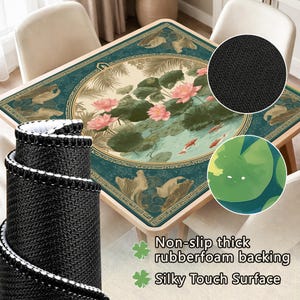 May include: A square table mat with a teal and beige floral design featuring pink lotus flowers, lily pads, and koi fish. The mat has a non-slip rubberfoam backing and a silky touch surface. A rolled-up black mat with white trim is in the foreground.