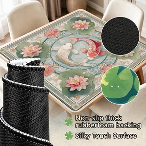 May include: A square table mat featuring a central circular design of two koi fish swimming in water, surrounded by pink lotus flowers and green lily pads. The mat has a black textured non-slip rubber foam backing and a smooth silky top surface.