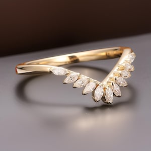 May include: A gold-colored ring with a curved design. The ring features a series of marquise-cut gemstones set along the curve, creating a fan-like arrangement. The ring's band is smooth and polished.