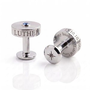 May include: A pair of silver-toned metal cufflinks. One cufflink features the name LUTHER engraved on the side and a small blue stone on top. The other cufflink displays a star engraving and the text To my husband, 15.10.10.2002, Lots of Love.