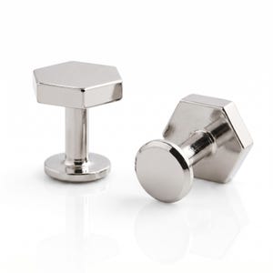 May include: A pair of silver-toned metal cufflinks featuring a polished hexagonal face and a cylindrical post with a circular base. The smooth, reflective surface of the metal catches the light, highlighting the geometric shape of the cufflink heads.