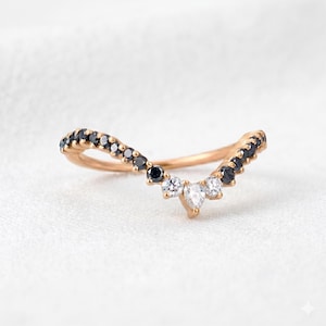 Puede incluir: Un anillo en forma de V hecho de oro rosa, con una serie de pequeñas piedras redondas negras engastadas a lo largo de la banda, que culmina en un grupo central de dos piedras blancas redondas y una piedra blanca en forma de pera.