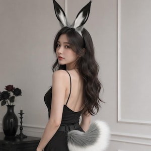 May include: A set of animal-inspired accessories including a headband with tall, pointed ears featuring black, white, and gray faux fur, and a matching fluffy, curved tail in white and gray attached to a black adjustable belt worn over a black dress.