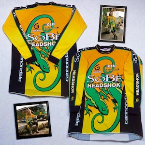 May include: Two long-sleeve jerseys featuring a yellow and black color scheme with a large green lizard graphic. The text "SOBE HEADSHOK" is printed on the front, along with "CLIF" and "SRAM" logos. Two framed photographs show a person wearing the jersey.