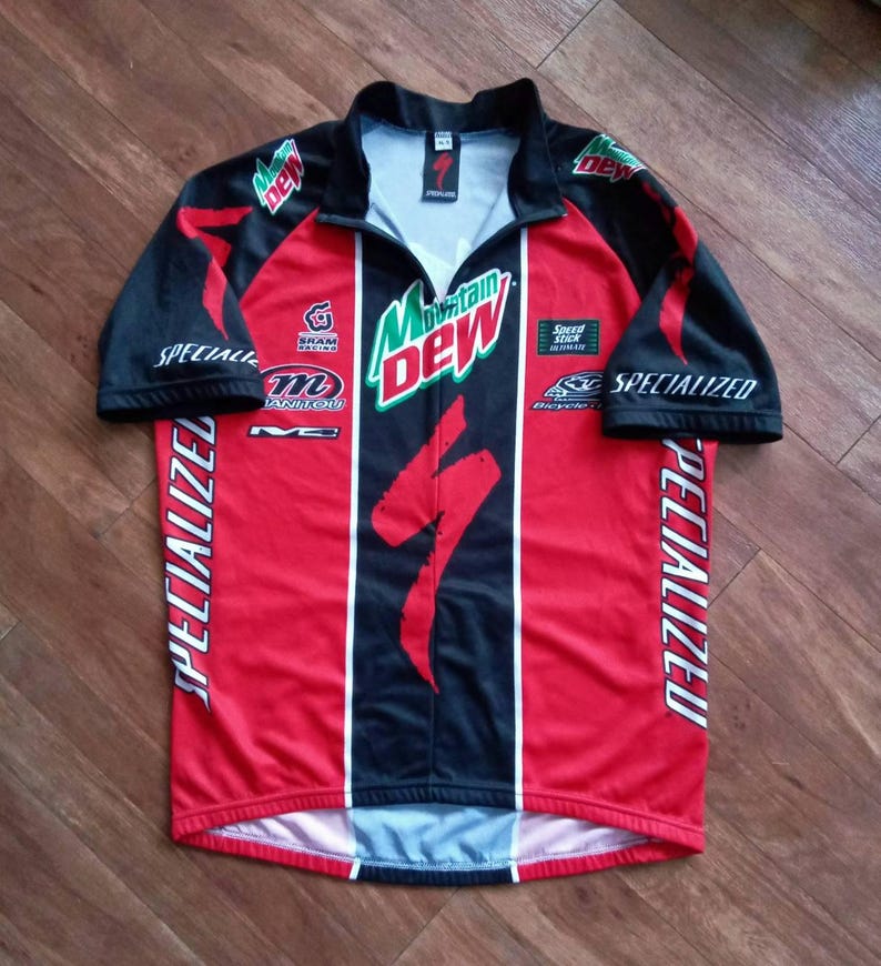 May include: A red and black Specialized cycling jersey with a half-zip collar. The jersey features the Mountain Dew logo, Specialized branding, and other sponsor logos. The sleeves are black, and the jersey has white vertical stripes down the front.