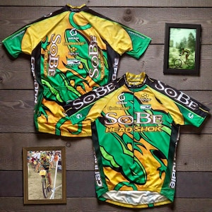 May include: Two short-sleeve cycling jerseys featuring a vibrant yellow and green lizard-like graphic pattern. The jerseys display the text SOBE and HEAD SHOK in bold white lettering, along with logos for SRAM, Continental, and Cannondale.