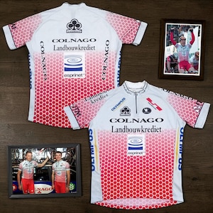 May include: Two white and red cycling jerseys featuring a honeycomb pattern, short sleeves, and a half-zip front. The jerseys display the Colnago, Landbouwkrediet, and Esprinet logos. Two framed photographs show cyclists wearing the same jersey design.
