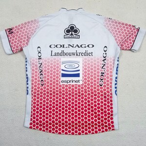 May include: A white short-sleeve cycling jersey featuring a red honeycomb pattern that fades from the bottom up. The jersey displays the text Colnago, Landbouwkrediet, and Esprinet, along with a black club logo and blue graphic elements on the sides.