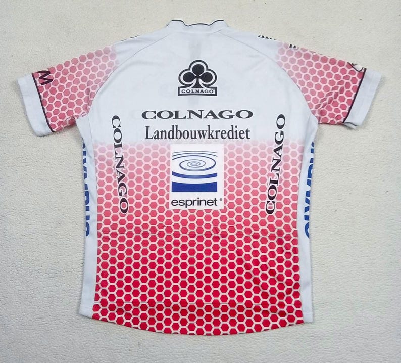 May include: A white short-sleeve cycling jersey featuring a red honeycomb pattern that fades from the bottom up. The jersey displays the text Colnago, Landbouwkrediet, and Esprinet, along with a black club logo and blue graphic elements on the sides.