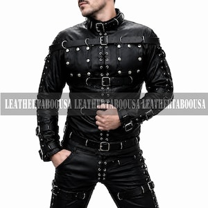 May include: A black leather jacket and matching pants set featuring silver-toned metal studs, multiple adjustable buckled straps, D-rings, and lace-up detailing along the sleeves and legs. The garment includes a high collar with a buckle.