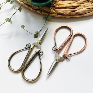 May include: Two pairs of decorative scissors with ornate handles. One pair is gold with a floral design and the other is copper with a geometric design.