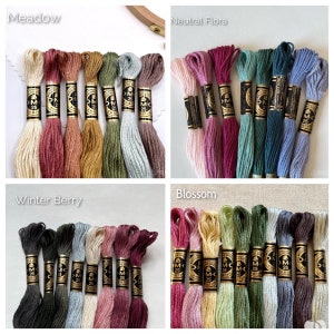 Puede incluir: Surtido de carretes de hilo de bordar DMC en varios colores, incluyendo beige, rosa, rojo, verde, azul y marr&oacute;n. El hilo est&aacute; organizado en cuatro grupos etiquetados como "Meadow", "Neutral Flora", "Winter Berry" y "Blossom".