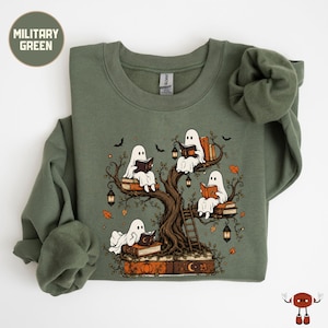 May include: A military green crewneck sweatshirt featuring a graphic print of four white ghosts sitting in a large tree, each reading a book. The tree is decorated with hanging lanterns, autumn leaves, and stacks of books at the base.