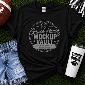 May include: A black short-sleeve t-shirt featuring a circular graphic with the text Grace House MOCKUP VAULT PREMIUM MOCKUPS for your business, established 2026, with a house and heart icon. The shirt has a crew neck and a standard fit.
