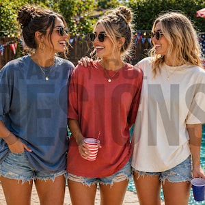 Op de afbeelding: Drie mensen dragen zonnebrillen en casual t-shirts in blauw, rood en crème, met spijkerbroekshorts. Ze staan bij een zwembad met een barbecue en een Amerikaanse vlag op de achtergrond. De scène suggereert een zomerse bijeenkomst.