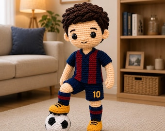 May include: A handmade crochet doll of a soccer player with dark brown hair, wearing a blue and red striped jersey with matching shorts, blue and red socks, and yellow shoes. The doll has one foot resting on a black and white soccer ball.