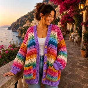 May include: A long-sleeve crochet cardigan featuring a vibrant horizontal striped pattern in shades of pink, orange, yellow, green, blue, and purple. The garment includes a solid purple trim, a V-neckline, two front pockets, and five wooden buttons.
