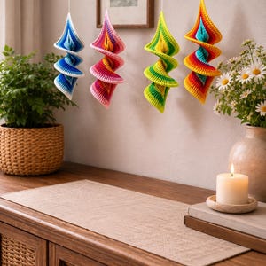 Puede incluir: Cuatro adornos colgantes en espiral hechos de hilo de ganchillo. El primero es azul y blanco, el segundo rosa y naranja, el tercero verde lima y amarillo, y el cuarto presenta un degradado de arco&iacute;ris vibrante en rojo, naranja, amarillo y azul.