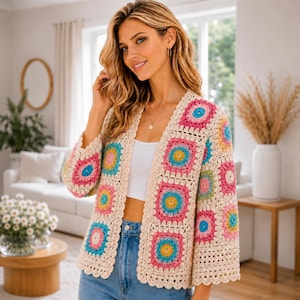 May include: A cream-colored, open-front crochet cardigan with colorful square patterns. The squares feature pink, blue, yellow, and green accents. The cardigan has three-quarter sleeves and a scalloped edge.