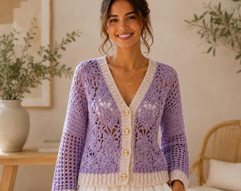 May include: A lavender crochet cardigan featuring a floral pattern, long sleeves, and a V-neckline with a cream-colored button-down placket. The garment has a cream-colored hem and cuffs, and is worn over a white garment.