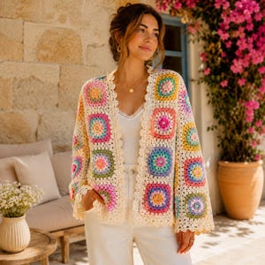 May include: A long-sleeved cardigan made of multi-coloured crochet granny squares in shades of pink, yellow, blue, and green, joined by cream-coloured yarn. The garment features an open front, a scalloped edge trim, and a loose, relaxed fit.