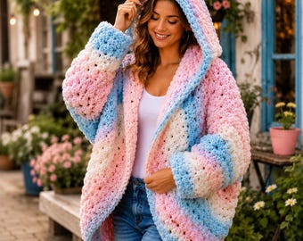 May include: A chunky knit hooded cardigan featuring a soft gradient pattern of pastel pink, white, and light blue yarn. The open-front garment has long sleeves and a relaxed fit, crafted from thick, textured yarn with a visible crochet-style stitch.