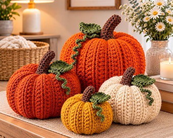 May include: A set of four crocheted pumpkins in orange, yellow, and cream colors. Each pumpkin features a dark brown stem and a green crocheted leaf with a curly vine. The pumpkins are arranged in a cluster on a textured surface.