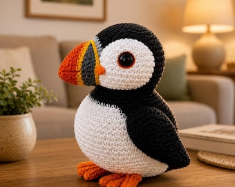 May include: A crochet puffin plush toy featuring a black and white body, a large black eye, and a multi-colored beak with segments of orange, yellow, and dark gray. The bird has bright orange feet and a rounded, soft-textured yarn construction.