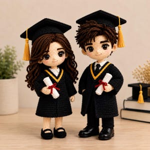 May include: Two crochet dolls dressed in black graduation gowns and caps with yellow tassels. Each doll has brown hair, light skin, and holds a white diploma tied with a red ribbon. The dolls wear black shoes and white collared shirts underneath.