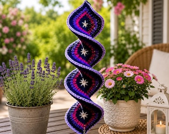 Puede incluir: Una decoración colgante de ganchillo en forma de espiral con un degradado de hilo azul oscuro, morado y magenta. La pieza está adornada con cuatro dijes de estrella plateados fijados en el centro y uno en la punta inferior.