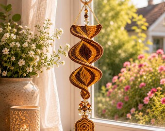 May include: A hanging spiral crochet ornament featuring alternating brown and golden-yellow yarn segments. The piece is suspended from a wooden ring and decorated with clear and brown beads, ending in a small, circular crochet flower motif.