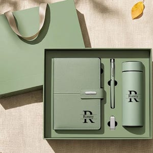 Op de afbeelding: Een saliegroene cadeauset bestaande uit een notitieboek met riemsluiting, een bijpassende pen en een cilindervormige thermosfles. Het notitieboek en de fles zijn gepersonaliseerd met de naam Ronny en de letter R. Een bijpassende tas is inbegrepen.