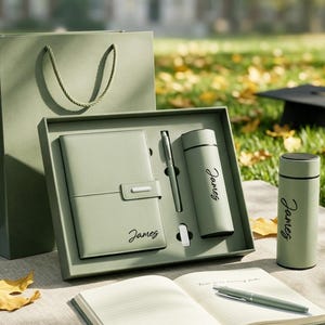 May include: A sage green gift set featuring a notebook, a pen, and a vacuum-insulated water bottle, all personalised with the name James. The set includes a matching gift bag and an open notebook with a pen resting on its lined pages.
