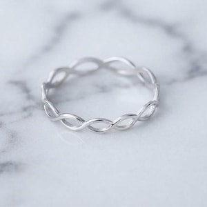 Op de afbeelding: Een ring van gepolijst zilver met een doorlopend, herhalend gedraaid metalen bandontwerp in infinity-stijl. De ring heeft een glad, reflecterend oppervlak en een cirkelvormige structuur met een delicaat en uniform patroon over de band.