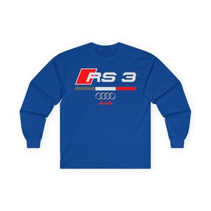 May include: A royal blue long-sleeve shirt featuring a graphic print on the chest. The design includes a red square with the white text RS 3, a horizontal gray, white, and red stripe, the silver Audi four-ring logo, and the red Audi wordmark.