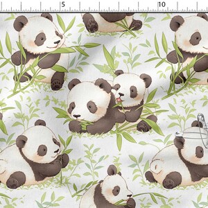 May include: White fabric featuring a repeating pattern of cartoon pandas. The pandas are black and white with brown accents, eating bamboo leaves. Green bamboo leaves and stems are scattered across the white background.